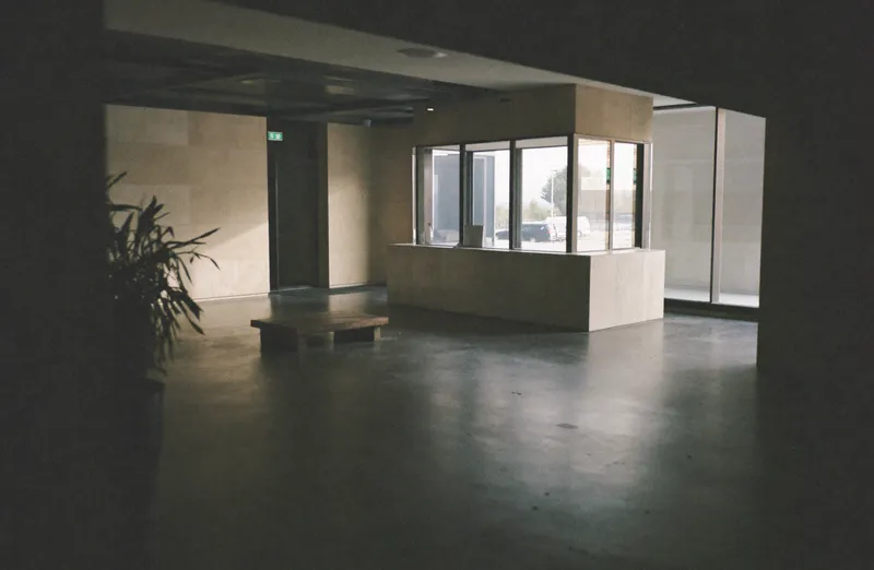 A quiet corporate office lobby in the early morning with an empty stone reception desk and daylight through a glass facade